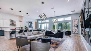 A spacious living area with a sofa, armchairs, and a coffee table. There is a kitchen in the background with white cabinets and a dining area. - Trendy Home w Trampoline RM, Bowling, Fantasy Themed BR & Theater - Near Disney (Davenport)