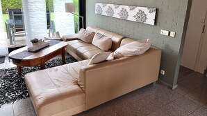 Ett modernt vardagsrum med en beige lädersoffa, ett träbord och en dekorativ väggdekoration.