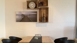 En matplats med ett träbord, två svarta stolar, en liten prydnad på bordet samt en väggklocka och en tavla ovanför bordet.