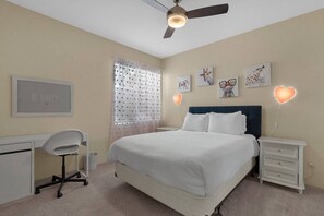 A bedroom with a bed, a desk, a chair, and a ceiling fan.