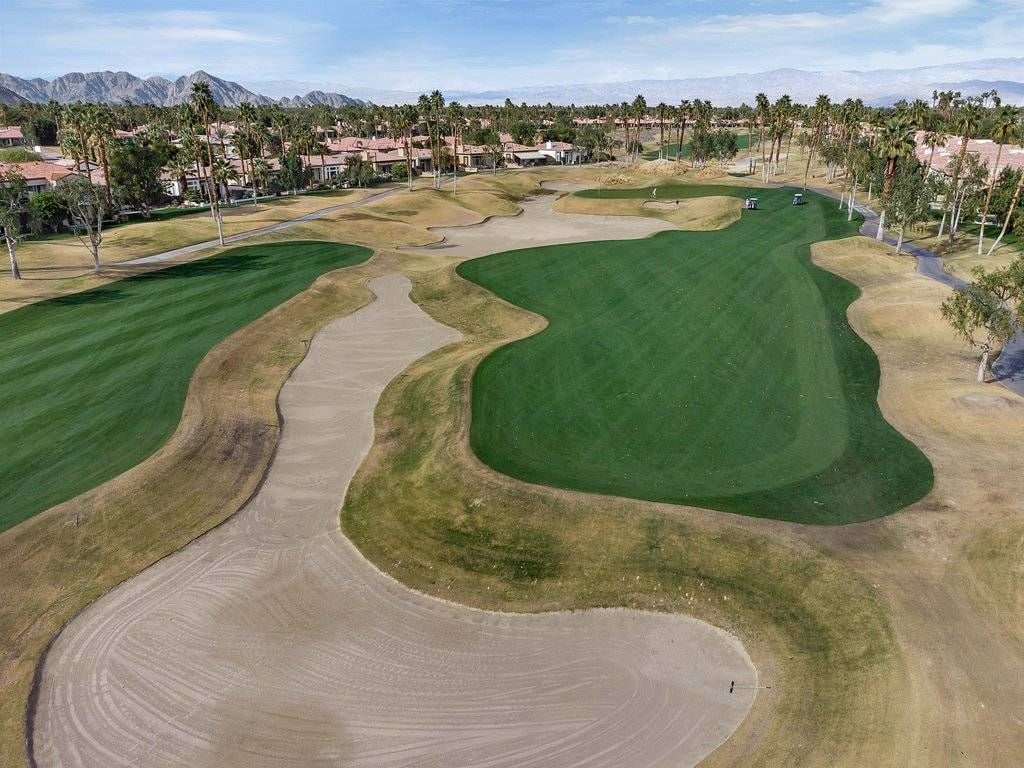 Ein Golfplatz mit Sandbunkern, Putting Green und Blick auf eine Wohngegend im Hintergrund.