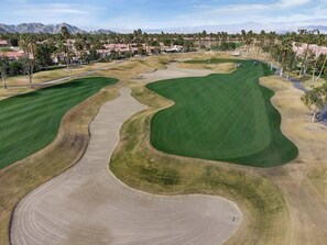 Un parcours de golf doté de bunkers de sable, d’un green d’entraînement et offrant une vue sur un quartier résidentiel en arrière-plan.