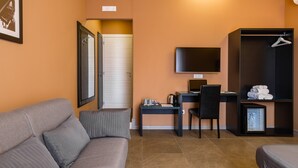 Una habitación de hotel moderna con un sofá gris, un escritorio con una computadora, un televisor y un armario.