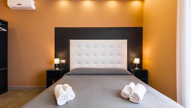 Una habitación de hotel con una cama grande, dos mesitas de noche con lámparas y un aire acondicionado instalado en la pared.