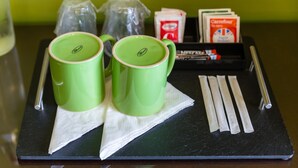 A tray with two green mugs, a napkin, straws, a pen, and some packaged food items. - BH Napoli Railway - Pistacchio - 4 (Napoli)