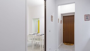 A hallway with a wooden door, white walls, and a dining area with white chairs and a table. - CasaNa on Christmas Alley (Napoli)