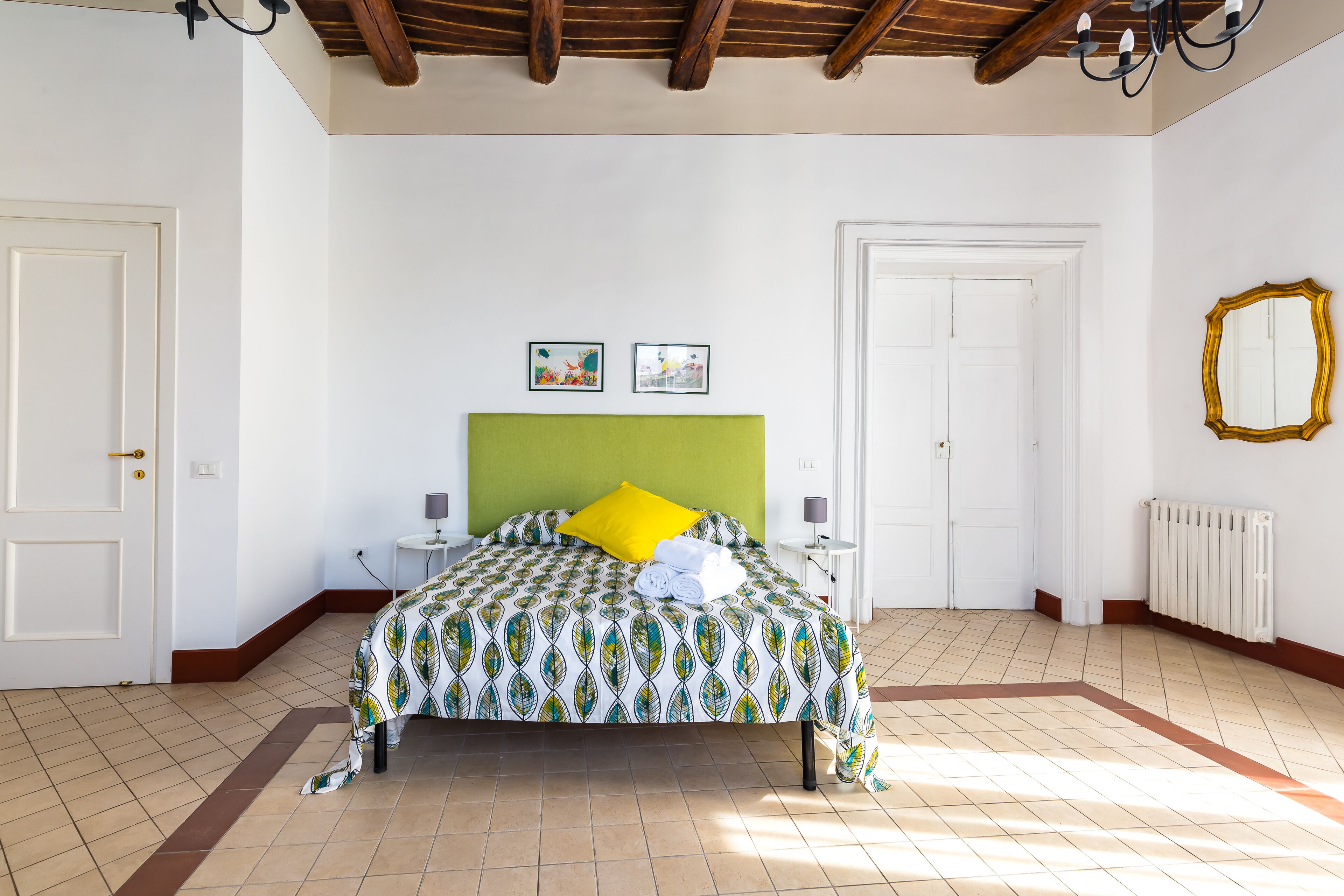 A bedroom with a bed, two bedside tables, a green headboard, and two framed pictures on the wall.