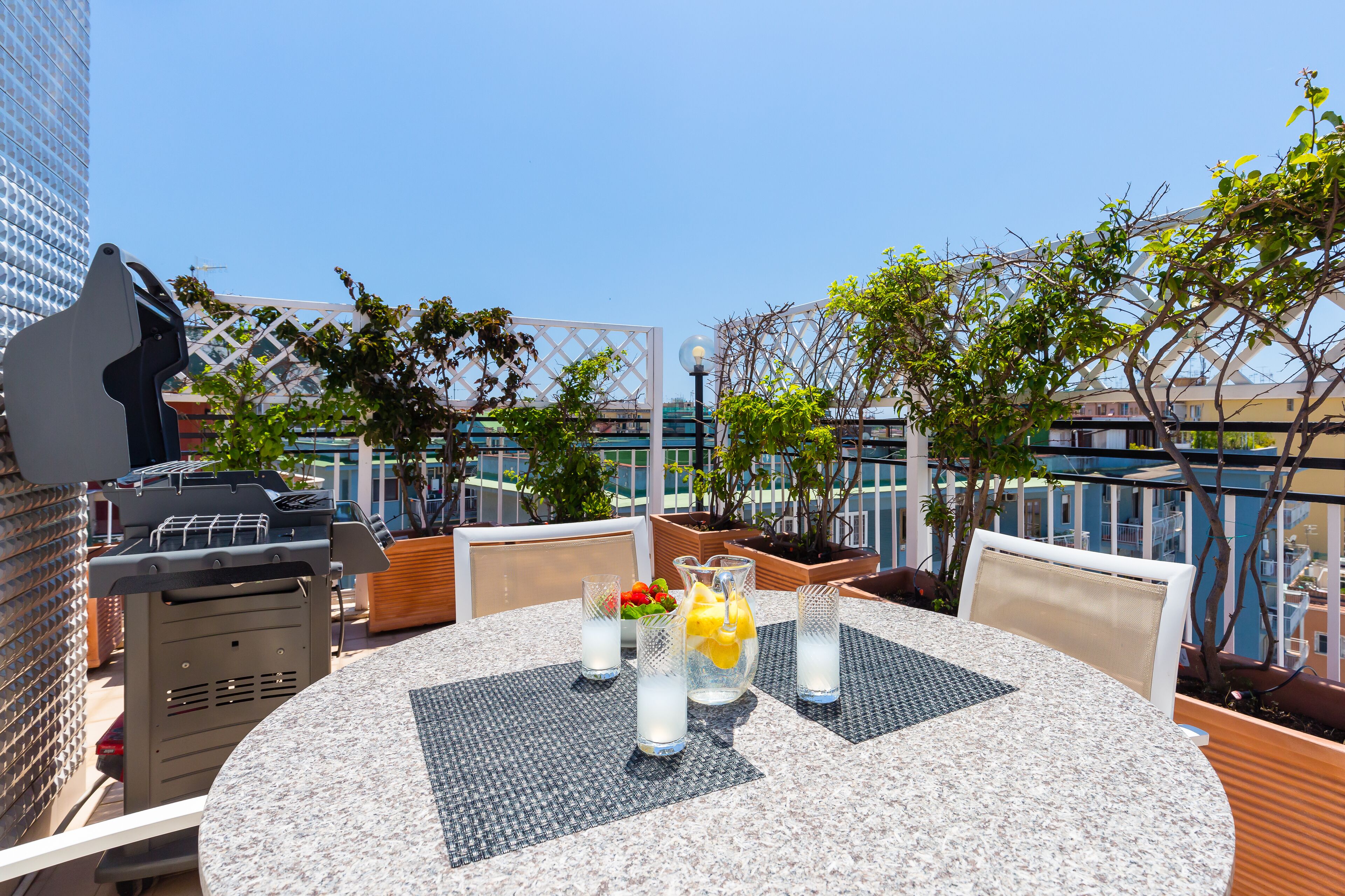 Une terrasse sur le toit avec une table ronde, des chaises, un barbecue et des plantes en pot.