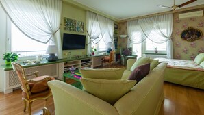A living room with a sofa, armchairs, a TV, a desk with a lamp, and a ceiling fan. - O-House Posillipo - Two Bedroom Apartment, Sleeps 6 (Napoli)
