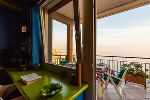 Ein Balkon mit Meerblick, ein Tisch mit gestreifter Tischdecke und ein Stuhl.