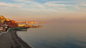 A coastal town with buildings along the waterfront, a pier extending into the water, and a mountain in the background. - O-House Posillipo - Two Bedroom Apartment, Sleeps 6 (Napoli)