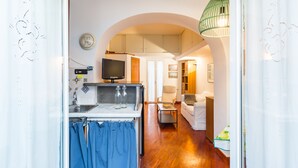 A compact kitchen with a built-in oven, a dining area with a white table and chairs, and a living room with a sofa and a TV. - Parthenope's Eye on the Seafront (Napoli)