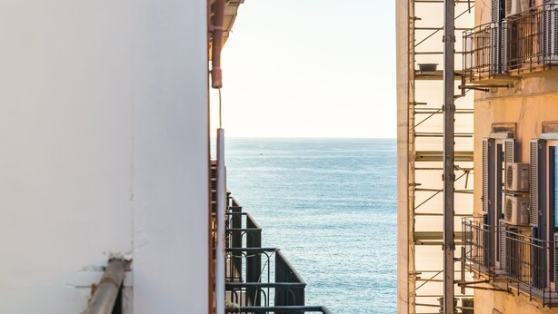 A view of the sea from a balcony with a metal railing and a building facade in the background. - Parthenope's Eye on the Seafront (Napoli)