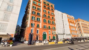 A multi-story building with a red facade and green shutters, featuring outdoor seating and a street view. - Parthenope's Eye on the Seafront (Napoli)