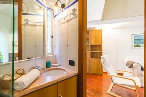 A bathroom with a marble sink, wooden cabinets, a towel, and a white chair. - Parthenope's Eye on the Seafront (Napoli)