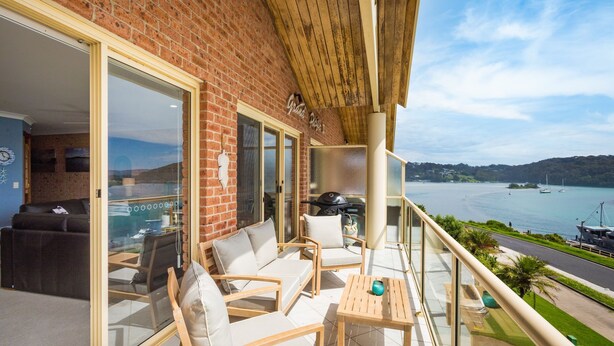 Un balcón con mobiliario de madera, una parrilla y vistas al mar y a los barcos.