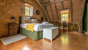 A rustic bedroom with a stone wall, wooden beams, a bed with white linens, a wooden nightstand, a desk, and a chair. - La Tour de Cause (Saint-Cybranet)