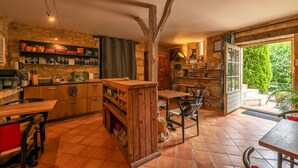 A rustic kitchen with wooden cabinets, a dining area with a table and chairs, and a view of greenery outside. - La Tour de Cause (Saint-Cybranet)
