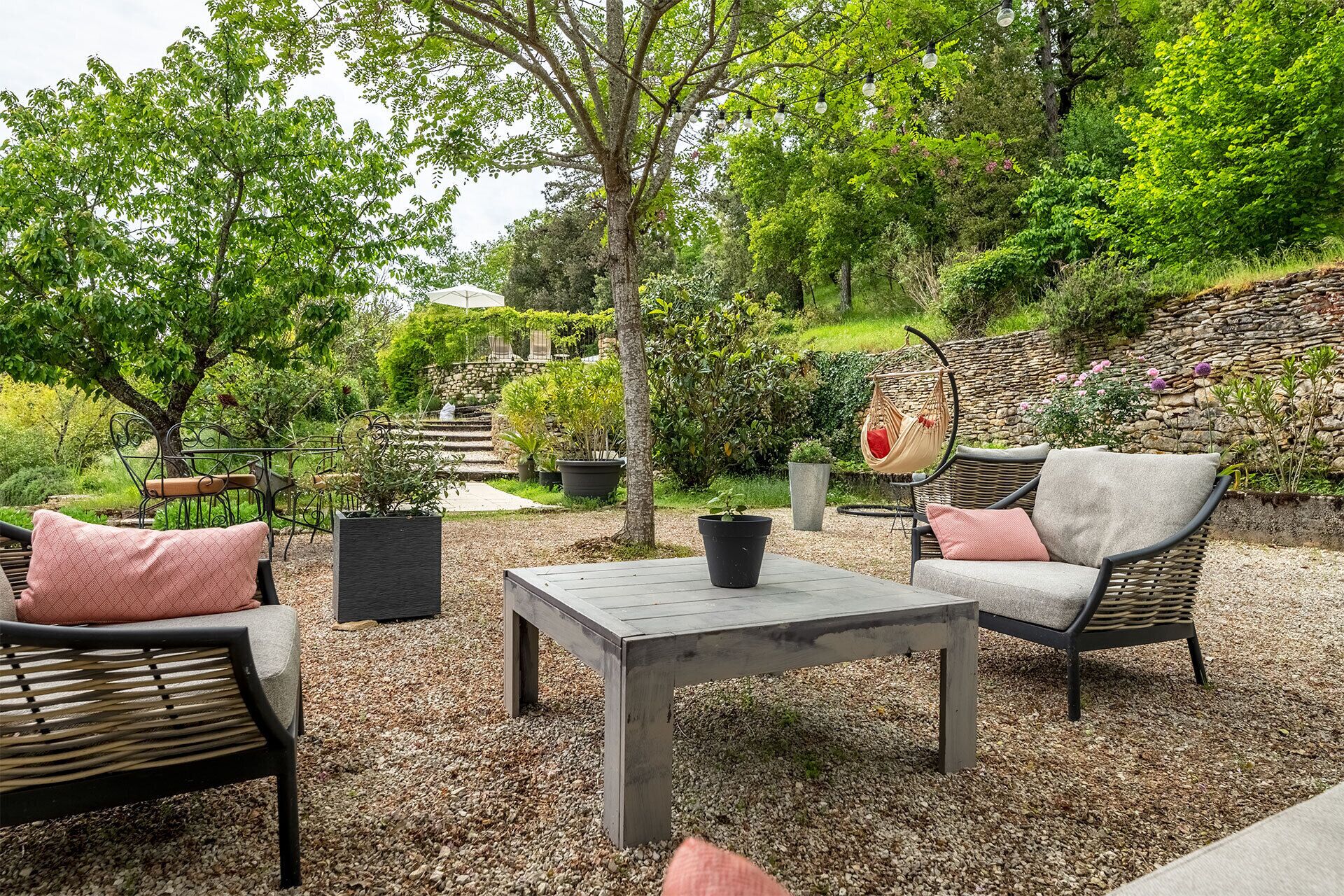 Een terras buiten met rieten meubels, een tafel en plantenpotten.
