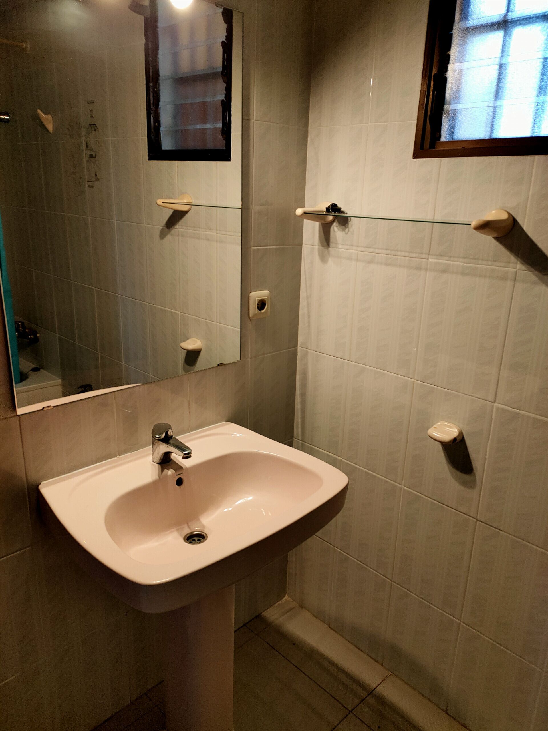 Un baño con lavamanos, espejo y paredes con azulejos.