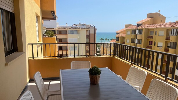 A balcony with a table and chairs, a potted plant, and a view of the sea and neighboring buildings. - Tamaris playa 7ºC Solo Familias! (Xeraco Playa)