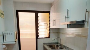Cocina compacta con armarios blancos, encimera de granito, lavamanos y horno empotrado.