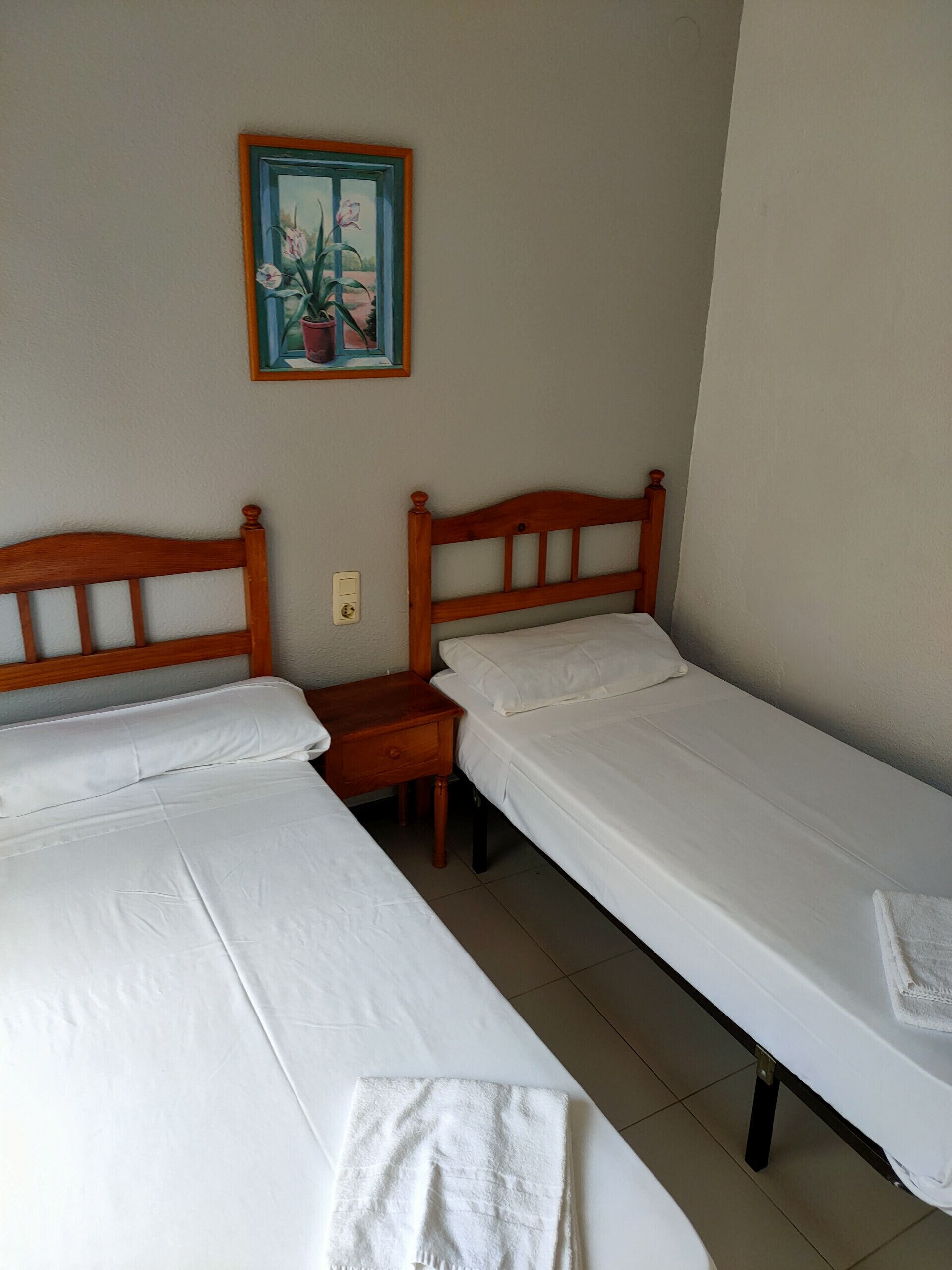 Una habitación con dos camas individuales, una mesita de noche de madera y un cuadro enmarcado en la pared.