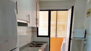 A compact kitchen with white cabinets, a built-in oven, a sink, and a microwave. - Tamaris playa 1ºD Solo Familias! (Xeraco Playa)