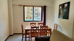 A dining area with a table and chairs, a window with curtains, and a sofa.