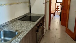 Una cocina con encimeras de granito, pileta de acero inoxidable, armarios de madera y un refrigerador.