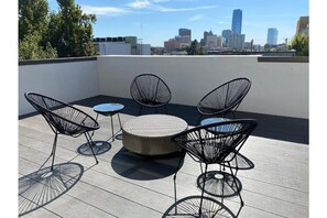 Une terrasse sur le toit, avec une table ronde et quatre chaises, et en arrière-plan, une vue sur les toits de la ville.