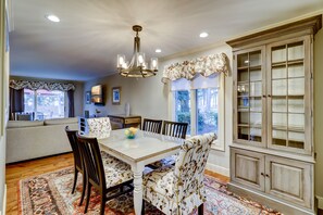 A dining area with a white table, floral upholstered chairs, and a patterned rug.