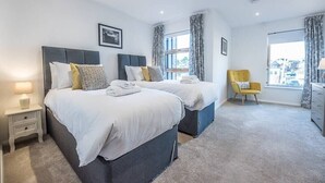 A modern hotel room with two beds, a small table, a chair, and a large window with curtains. - 2 Deben Wharf, Woodbridge (Woodbridge)