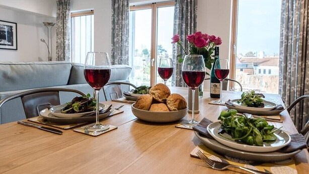 A dining table set with plates of food, glasses of red wine, and a vase of flowers. - 2 Deben Wharf, Woodbridge (Woodbridge)