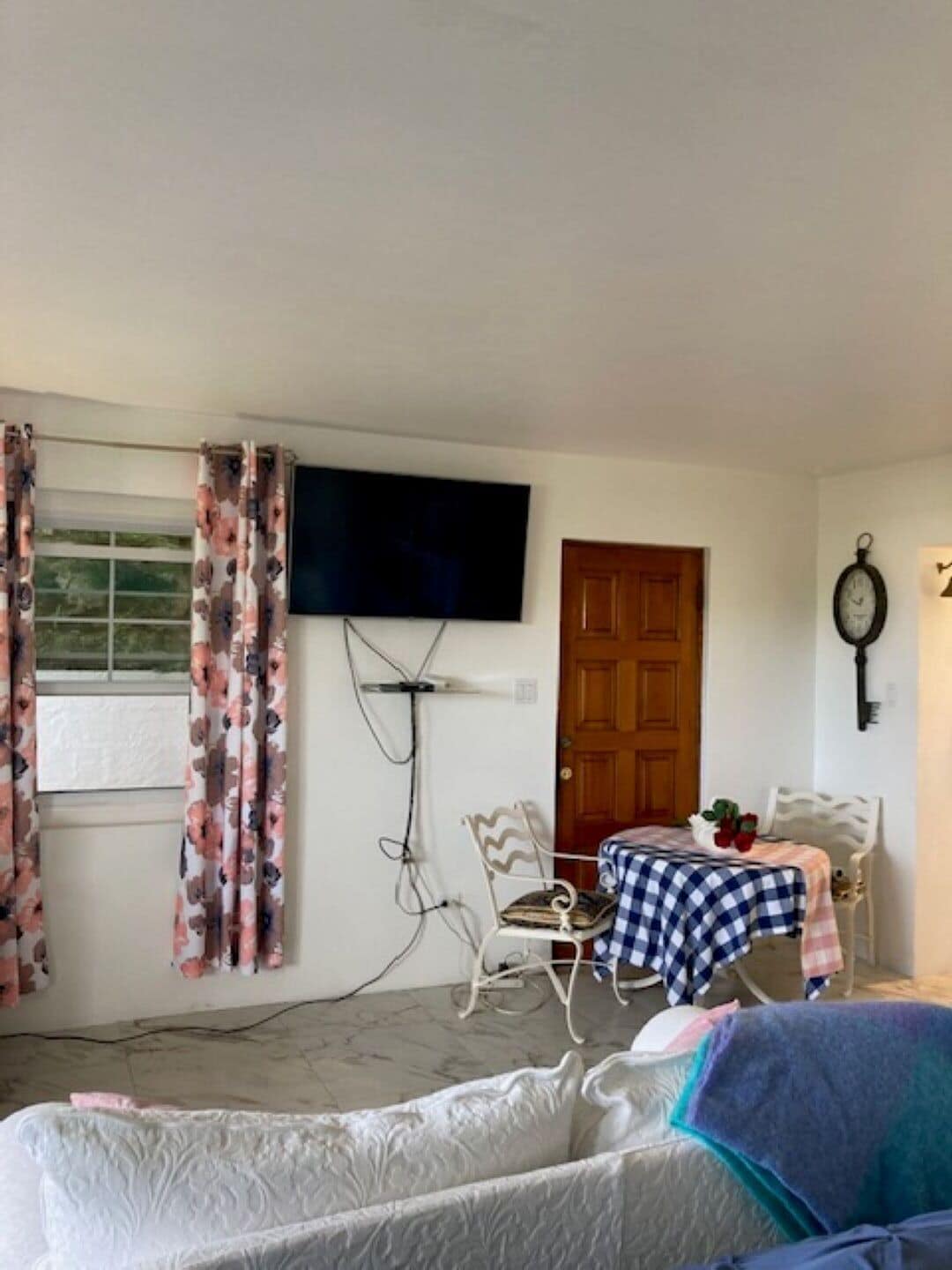 Ein Schlafzimmer mit einem Bett, einem an der Wand montierten Fernseher, einer Holztür und einem kleinen Tisch mit kariertem Tischläufer.