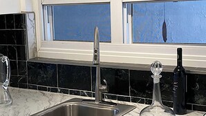 A kitchen with a double sink, a stove, and a window with blue-tinted glass. - [A]MOUR AMOUR AMOUR

Lighthouse Views • Walk to Beaches • Classic Bermuda Charm (Hamilton)