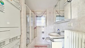 Une petite salle de bain comprenant un lave-linge, un évier et un radiateur.