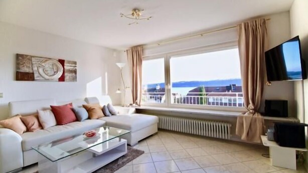 Un salon moderne avec un canapé blanc, une table basse en verre et une grande fenêtre agrémentée de rideaux.