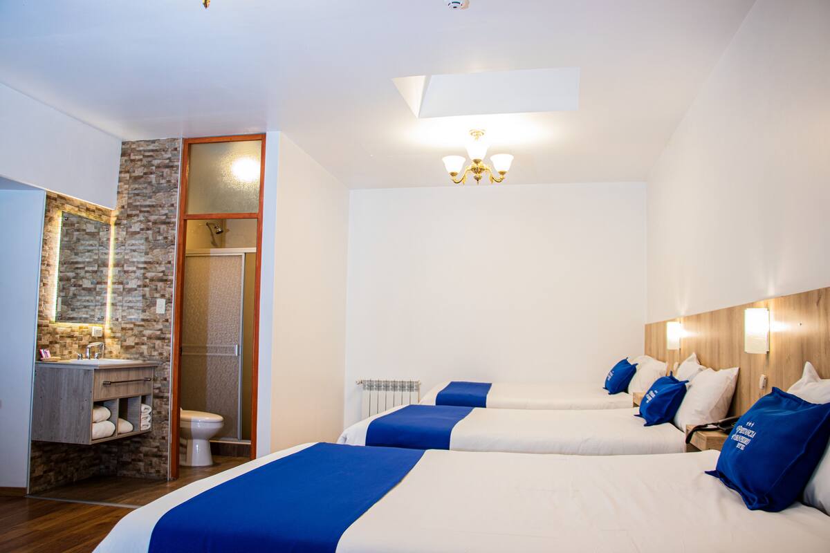 Ein Hotelzimmer mit drei Betten, einem Badezimmer mit Steinwand und einer Kristallleuchter.