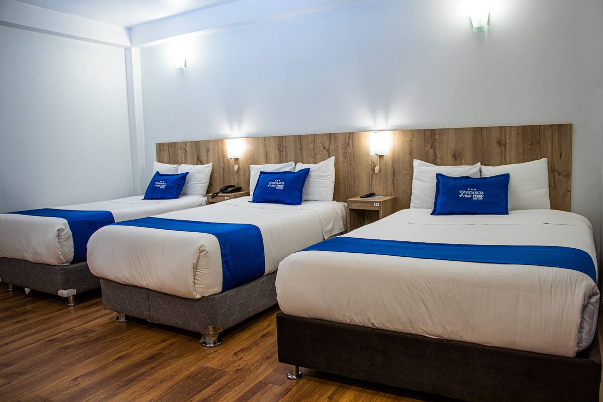 Drei Betten mit blau-weißer Bettwäsche, Holz-Kopfteilen und Nachttischlampen.