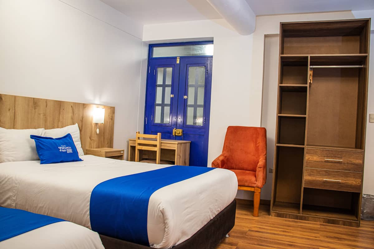Ein Hotelzimmer mit zwei Betten, einem Holz-Kopfteil, einer blauen Tür, einem roten Sessel und einem begehbaren Kleiderschrank.