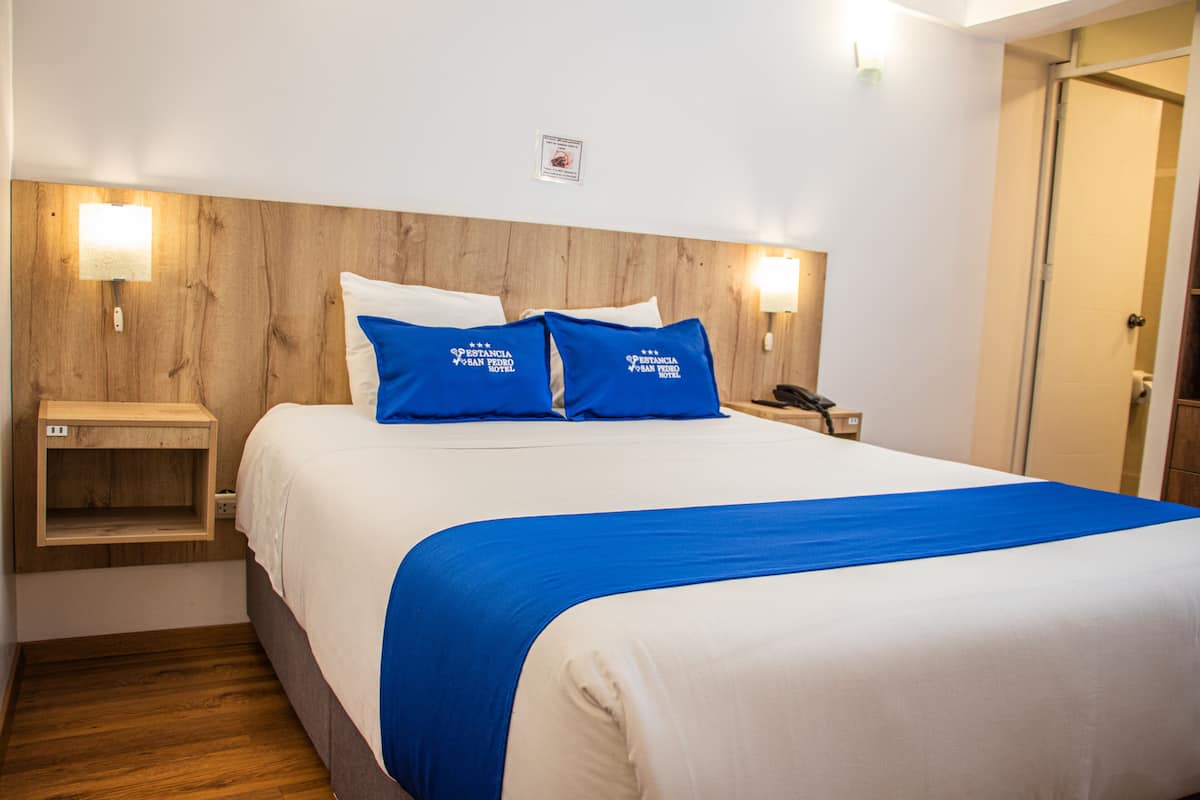 Ein Hotelzimmer mit Holz Kopfteil, einem Bett mit weißer und blauer Bettwäsche, zwei Nachttischlampen und einem Nachttisch aus Holz.