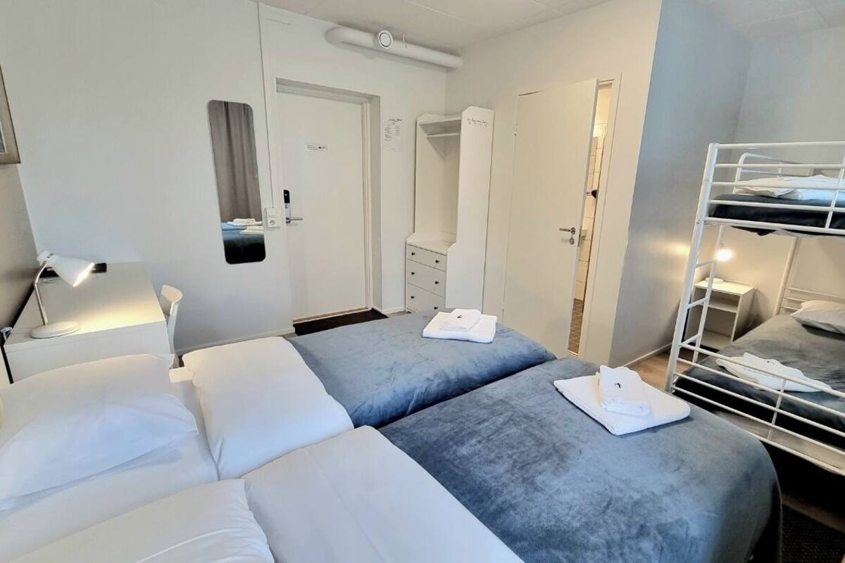 Une chambre d’hôtel avec deux lits, un bureau avec une lampe, une armoire et un lit superposé.