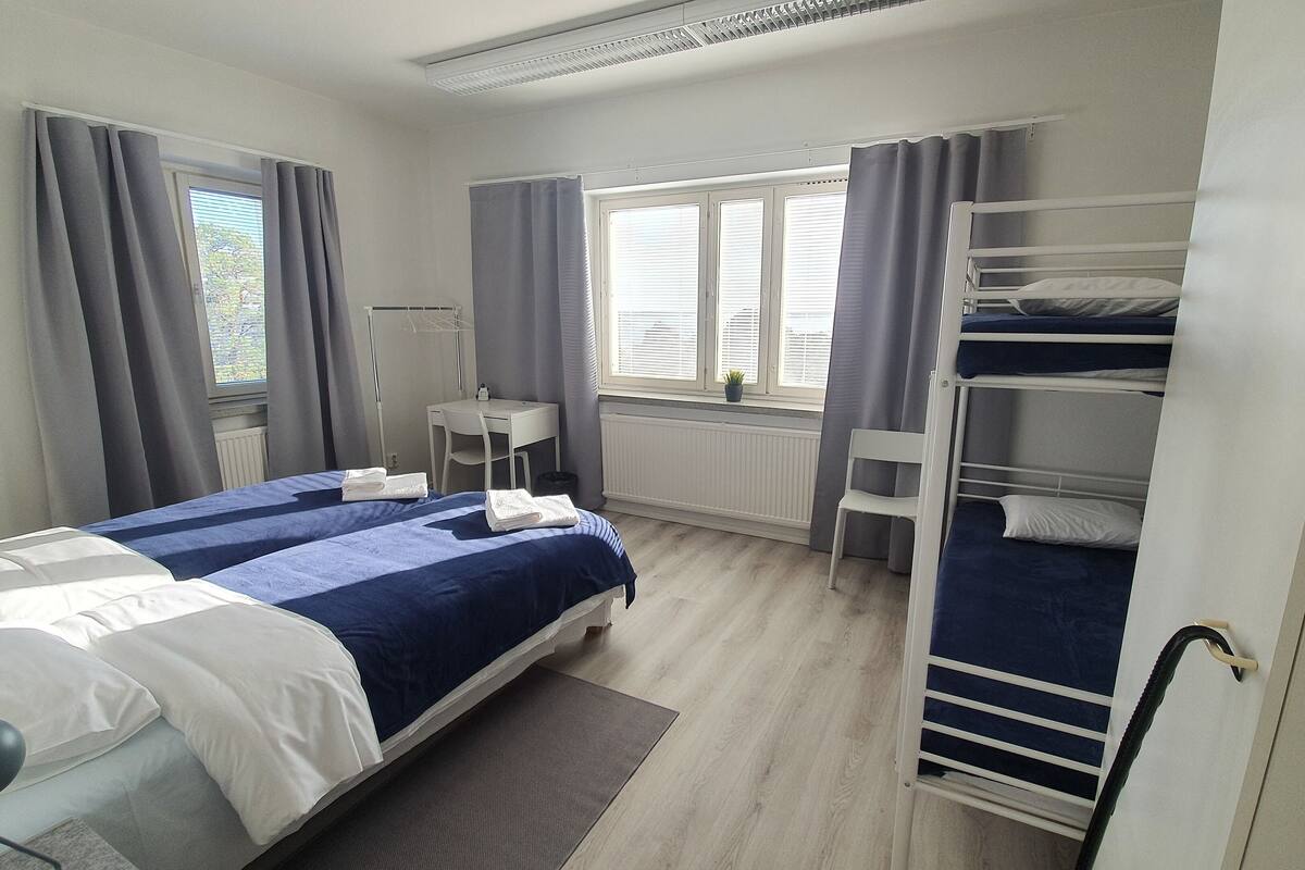 Une chambre d’hôtel avec un lit, un bureau, une chaise, un radiateur et une fenêtre avec des rideaux.