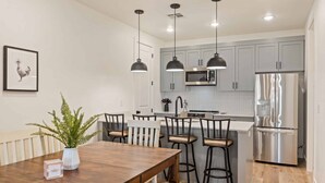 A modern kitchen with grey cabinets, stainless steel appliances, pendant lighting, and a wooden dining table with chairs. - Adventures at the Cowabungalow: Desert Color Lagoon + Beaches (St George)