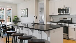 A modern kitchen with white cabinets, a stainless steel stove, and a black countertop island with bar stools. - 1 Dreamy Place: Waterslide+ Lazy River, Dog-Friendly (Washington)