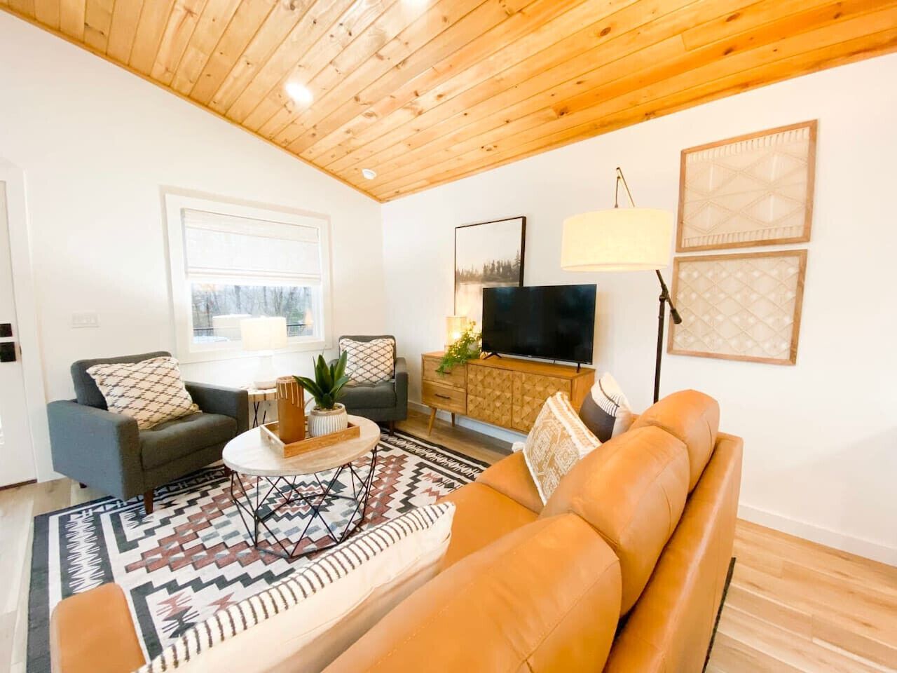 A living room with a wooden ceiling, a sofa, a coffee table, a TV, and a patterned rug.