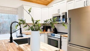 A modern kitchen with white cabinets, stainless steel appliances, and a wooden island with a white vase. - The Aerie ~ A Modern Retreat at Double Bridges (Mountain View)