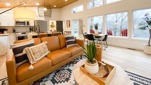 A modern living room with a brown leather sofa, a patterned rug, and a dining area with a table and chairs. - The Aerie ~ A Modern Retreat at Double Bridges (Mountain View)
