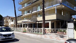 Ein mehrstöckiges Hotel mit Balkonen, einem überdachten Eingang und einem weißen Auto vor der Fassade.